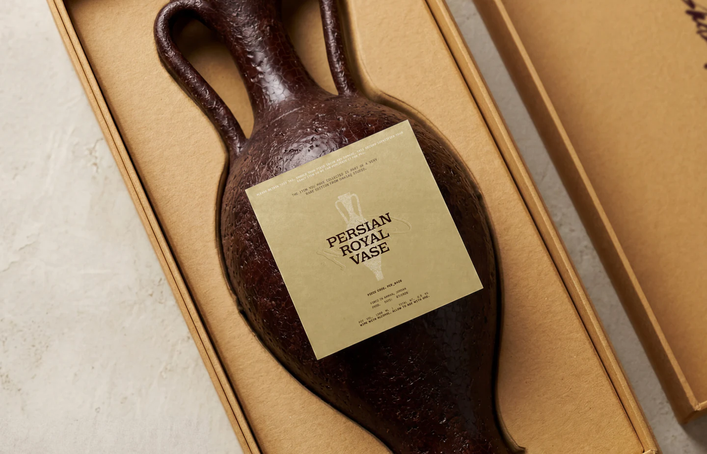A dark clay vase in its box with a sand label